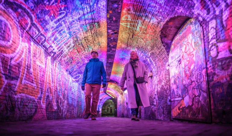 Twee mensn lopen door een verlichte tunnel in Utrecht - onderdeel van lichtkunstwerkenroute Utrecht Lumen